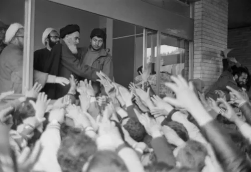 المرشد روح الله الخميني يحيي حشوداً من المتظاهرين خلال الثورة الإسلامية عام 1979 التي أطاحت بالشاه المدعوم أمريكياً، مع التركيز على التحولات السياسية في إيران.