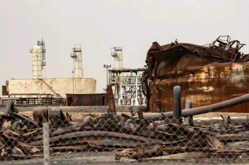 صورة لموقع انفجار في دير الزور، يظهر فيه حطام حافلة متضررة ومنشآت نفطية خلفها، بعد هجوم أسفر عن مقتل أربعة من عناصر الأمن.