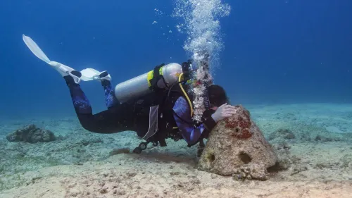 غواص يتفاعل مع قاع المحيط، محاطًا بفقاعات الهواء، في إطار يبرز جمال الحياة البحرية وأهمية الغوص.