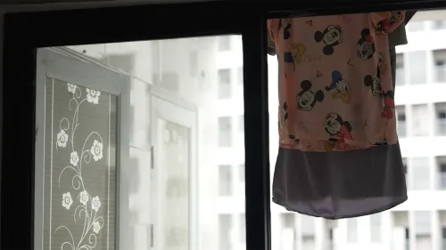 قميص أطفال يحمل رسومات ميكي ماوس معلق على نافذة، يرمز إلى غياب الأمهات بسبب الاتجار بالبشر في الفلبين.