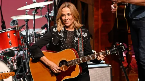 شيريل كرو تعزف على الغيتار خلال عرض موسيقي، مع خلفية من الطبول، تعبيرًا عن احتجاجها على إيلون ماسك.