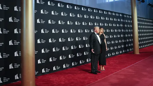 دونالد ترامب وميلانيا ترامب يقفان على السجادة الحمراء في مركز كينيدي، مع خلفية تحمل شعار المركز، خلال حدث ثقافي مثير للجدل.