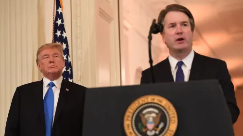 دونالد ترامب يقف خلف ميكروفون أثناء خطاب القاضي بريت كافانو في حفل التنصيب، مع العلم الأمريكي خلفهم، مشيراً إلى التحولات السياسية في المحكمة العليا.