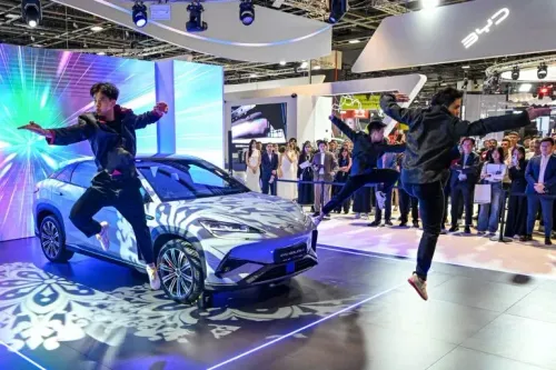 عرض لسيارة كهربائية من BYD في صالة عرض حديثة، مع راقصين يؤدون عرضًا مبهجًا في خلفية ملونة، وسط حشد من الزوار.