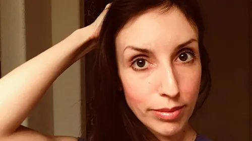 امرأة شابة تحمل شعرًا بنيًا، تلمس شعرها، وتظهر تعبيرًا هادئًا. الصورة تتعلق بمخطط احتيالي استهدف رجالًا مسنين عبر تطبيقات المواعدة.