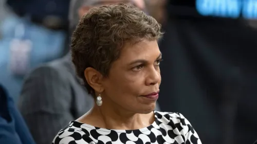 امرأة ذات شعر قصير ومجعد، ترتدي فستانًا بنمط مميز، تبدو في حالة تفكير خلال جلسة استماع قانونية تتعلق بإدارة ترامب.