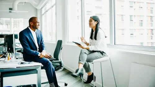 محادثة بين رجل وامرأة في مكتب حديث، حيث يتبادلان الحديث بشكل ودي، مما يعكس أهمية التواصل الاجتماعي.