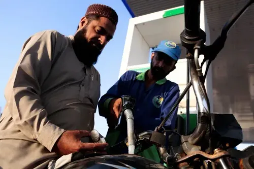 رجل يملأ دراجته النارية بالوقود في محطة، بينما يعمل موظف على مساعدته، مما يعكس تأثير ارتفاع أسعار الوقود على الحياة اليومية في باكستان.