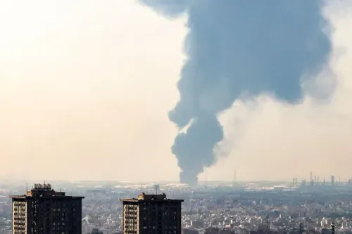 تصاعد دخان كثيف من منطقة صناعية في طهران، مما يشير إلى انفجارات أو هجمات، مع وجود مباني سكنية في المقدمة.