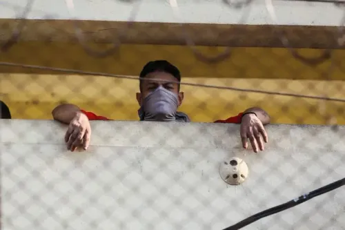 سجين ملثم يراقب من فوق جدار سجن رينوفاسيون 1 في غواتيمالا، وسط توتر بعد أعمال شغب منسقة من قبل العصابات.