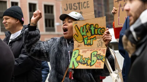 محتجّة تحمل لافتة تطالب بالعدالة لروبرت بروكس، مع تعبير عن الغضب في مظاهرة ضد العنف في السجون.