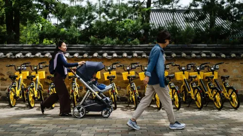 امرأة تدفع عربة أطفال بينما تسير بجانب صف من الدراجات الصفراء في كوريا الجنوبية، تعكس الزيادة في الزيجات والخصوبة.