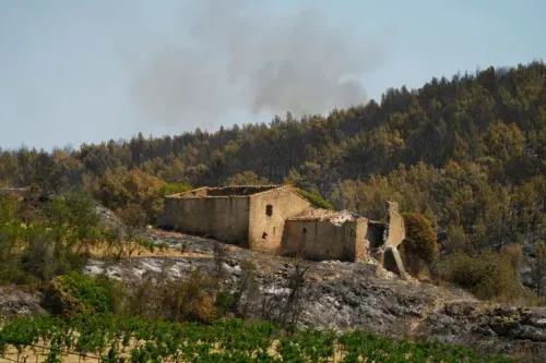 دخان يتصاعد من منطقة حريق في جنوب فرنسا، حيث تظهر بقايا منزل محترق وسط غابة دمرتها النيران، مما يعكس تأثير موجة الحر.