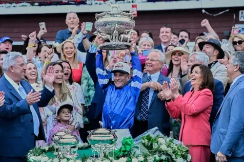 جونيور ألفارادو يحتفل بفوز "سوفرينتي" بسباق بلمونت ستيكس، محاطًا بالجمهور والمشجعين، وهو يحمل الكأس الفضي.