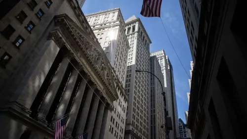 واجهة بورصة نيويورك مع أعمدة معمارية بارزة، بينما ترفرف علم الولايات المتحدة في السماء الزرقاء، تعكس أهمية السوق المالي.