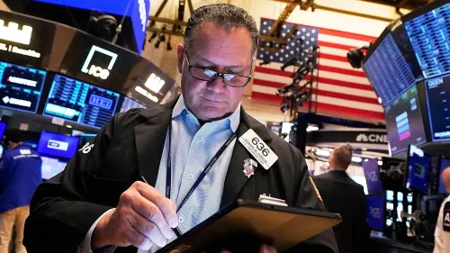تاجر في بورصة نيويورك يتابع الأسهم ويكتب ملاحظات، مع ظهور شاشات التداول والخلفية الوطنية الأمريكية.