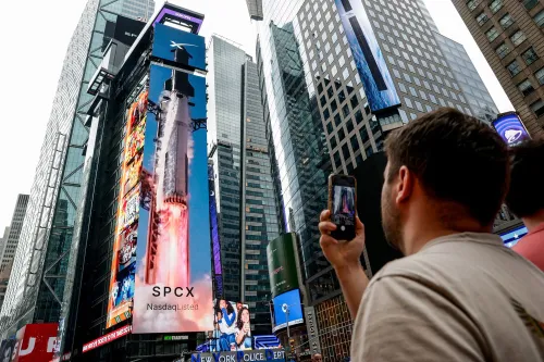 شخص يلتقط صورة لهاتفه لعرض SpaceX الضخم في تايمز سكوير، الذي يبرز تقييم الشركة المرتفع وأحدث صفقة استحواذ لها.