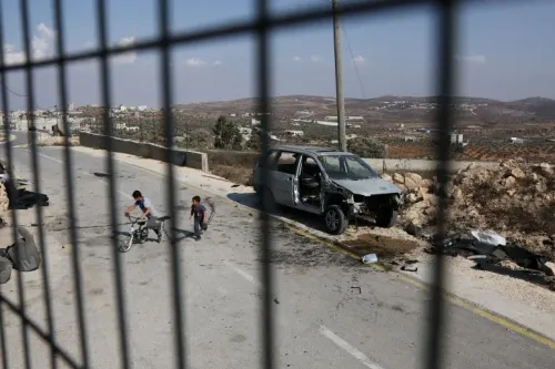 أطفال فلسطينيون يلعبون قرب سيارة محطمة على طريق في الضفة الغربية، في ظل تصاعد التوترات والاحتلال الإسرائيلي والضم غير المشروع.