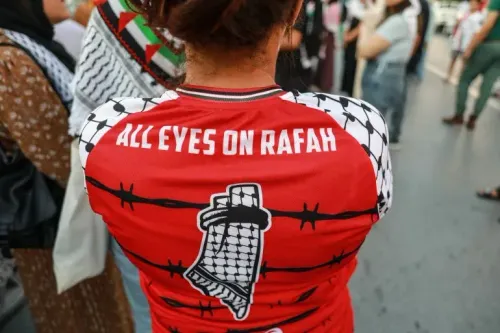 قميص أحمر يحمل عبارة "كل الأنظار على رفح" مع رسومات تعكس الوضع في غزة، وسط تجمع شعبي للتضامن مع الفلسطينيين.