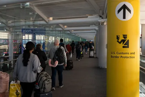 طابور من المسافرين في مطار أمريكي، متجهين نحو نقطة تفتيش الجمارك وحماية الحدود، مع لافتة تشير إلى الاتجاه.