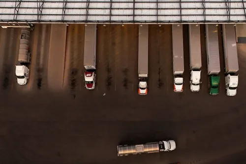 صف من الشاحنات التجارية متوقفة في ساحة، مع شاحنة واحدة تتحرك في الاتجاه المعاكس. تعكس الصورة الوضع الحالي لصناعة النقل.