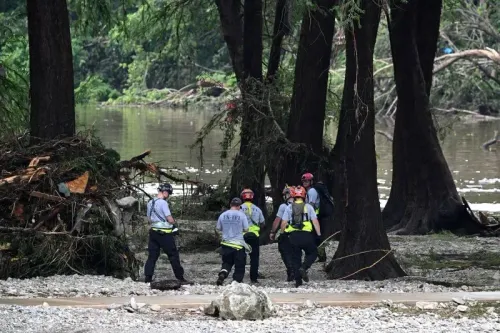 فرق الإنقاذ تعمل في موقع مخيم ميستيك بعد الفيضانات، مع وجود حطام وأشجار قرب نهر غوادالوبي، مما يعكس الأضرار الكبيرة.