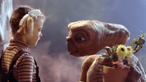 مشهد شهير من فيلم "E.T. the Extra-Terrestrial" يظهر طفلة تواجه الكائن الفضائي E.T. وهو يحمل زهورًا، مع تفاعل مليء بالبراءة والدهشة.