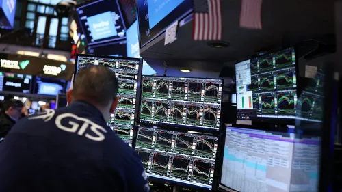 تظهر الصورة تاجرًا في سوق الأسهم محاطًا بشاشات تعرض بيانات السوق، مما يعكس تأثير الرسوم الجمركية على الاقتصاد.