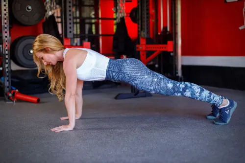 امرأة تؤدي تمرين الضغط في صالة رياضية، مما يعزز قوة عضلات الكتف. التركيز على تقنيات التنفس لتحسين الثبات والوضعية.