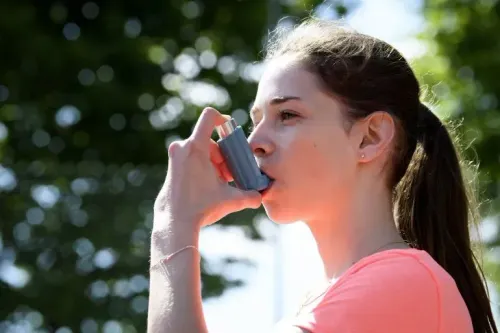 فتاة تستخدم جهاز استنشاق لعلاج الربو في الهواء الطلق، مما يسلط الضوء على تأثير أجهزة الاستنشاق على البيئة وانبعاثات الكربون.