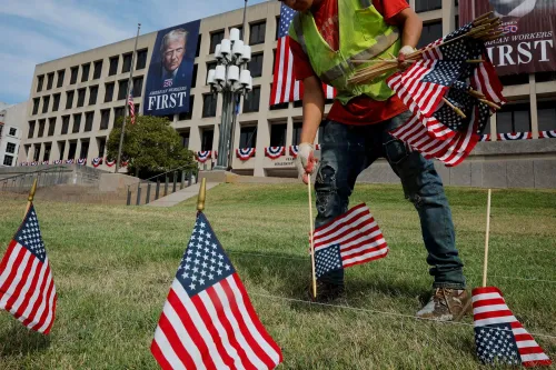 عامل يزرع أعلامًا أمريكية صغيرة أمام مبنى حكومي مزين بشعار "العمال الأمريكيون أولاً" بمناسبة عيد العمال.