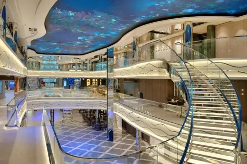 تصميم داخلي حديث لسفينة سياحية، يظهر سلالم زجاجية وأسطح ملونة، مع إضاءة نيون، تعكس الفخامة والتكنولوجيا المتقدمة في الرحلات البحرية.