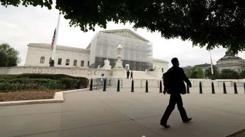 رجل يرتدي بدلة يسير بجوار المحكمة العليا الأمريكية، التي تظهر مغطاة بشبكة حماية، مع وجود أعمدة ومجموعة من السياج في الخلفية.