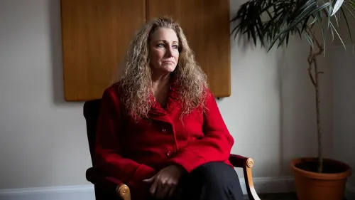 امرأة تجلس في غرفة مضاءة بشكل خافت، ترتدي سترة حمراء، تعبر عن مشاعر القلق أو التأمل، في سياق قضية قانونية حول التمييز في العمل.