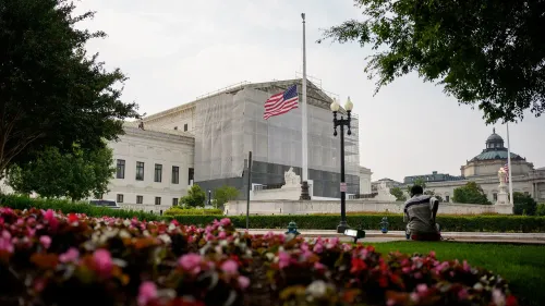 مبنى المحكمة العليا مغطى بشبكة، مع العلم الأمريكي يرفرف في الهواء، وشخص جالس في الحديقة وسط الأزهار.