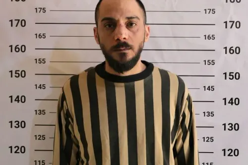 صورة للمشتبه به الرئيسي في مجزرة تضامن، يظهر في ملابس مخططة، مع آثار كدمات على وجهه، خلفه خلفية قياس الطول.