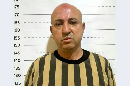 وسيم الأسد أمام خلفية قياس الطول، مدان بجرائم حرب في سوريا وحكم عليه بالإعدام في محاكمة تاريخية.