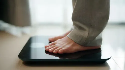 قياس محيط الخصر باستخدام ميزان ذكي، حيث تظهر قدمي شخص يرتدي بنطالًا رماديًا، مما يعكس أهمية الصحة البدنية وتأثيرها على صحة الدماغ.