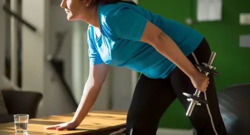 امرأة تمارس تمارين القوة باستخدام الدمبل، مع التركيز على الحفاظ على وضعية صحيحة، في بيئة منزلية.