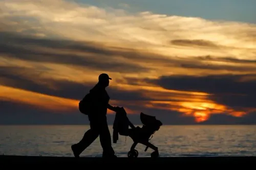 أب يتجول مع عربة أطفال على شاطئ عند غروب الشمس، مما يعكس القلق المتزايد بشأن ارتفاع أسعار مستلزمات الأطفال بسبب التعريفات الجمركية.