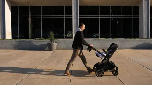 رجل يدفع عربة أطفال على الرصيف أمام مبنى، مما يعكس تأثير ارتفاع الأسعار على مستلزمات الأطفال وسط التغيرات الاقتصادية.