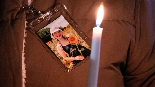 صورة لامرأة تحمل شمعة مضاءة، مع صورة لها تظهر وهي تحمل زهرة دوار الشمس، تعكس لحظة تأمل في ذكرى مؤلمة.