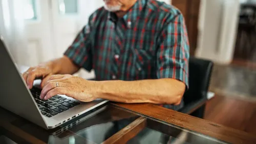 رجل مسن يجلس أمام جهاز كمبيوتر محمول، يستخدم التكنولوجيا في بيئة منزلية، مما يعكس تأثيرها على الصحة المعرفية.