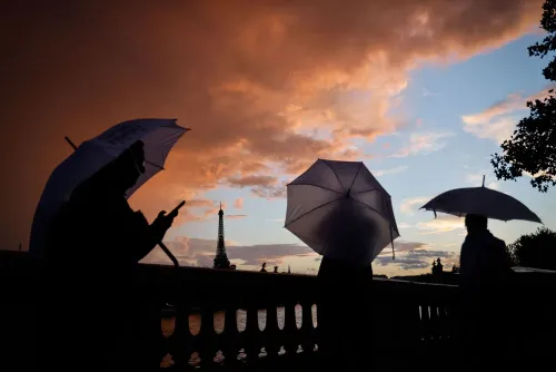 أشخاص يحملون مظلات في غروب الشمس، مع معالم بارزة مثل برج إيفل في الخلفية، مما يعكس جمال الحياة في الخارج.