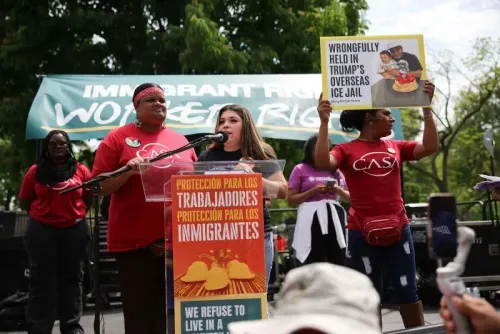 نساء يتحدثن في تجمع لدعم حقوق المهاجرين، مع لافتة تشير إلى احتجاز غير قانوني لأحد الأشخاص في سجون ترامب.