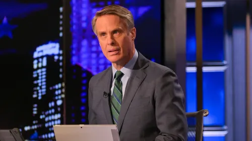 تيري موران يتحدث بجدية أثناء تقديمه برنامجًا إخباريًا، مع خلفية مضاءة تعكس أجواء استوديو التلفزيون.