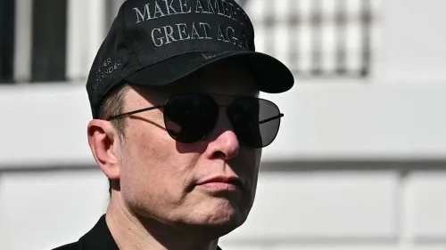 إيلون ماسك يرتدي نظارات شمسية وقبعة تحمل عبارة "اجعل أمريكا عظيمة مرة أخرى"، يعكس التوترات حول إدارة تسلا وأدائها.