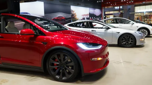 سيارات تسلا الكهربائية تتواجد في صالة عرض، مع سيارة حمراء بارزة في المقدمة، تعكس التنافس المتزايد في سوق السيارات الكهربائية.