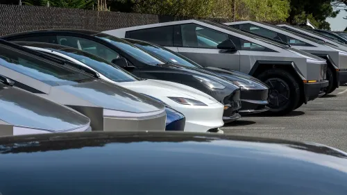 تظهر الصورة مجموعة من سيارات تيسلا الكهربائية، بما في ذلك الطراز Y والطراز الجديد Cybertruck، في موقف سيارات.