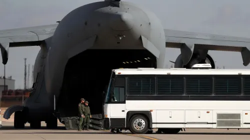 طائرة شحن عسكرية كبيرة في قاعدة فورت بليس، مع حافلة تنتظر لنقل المهاجرين المحتملين إلى منشآت الإيواء الجديدة.